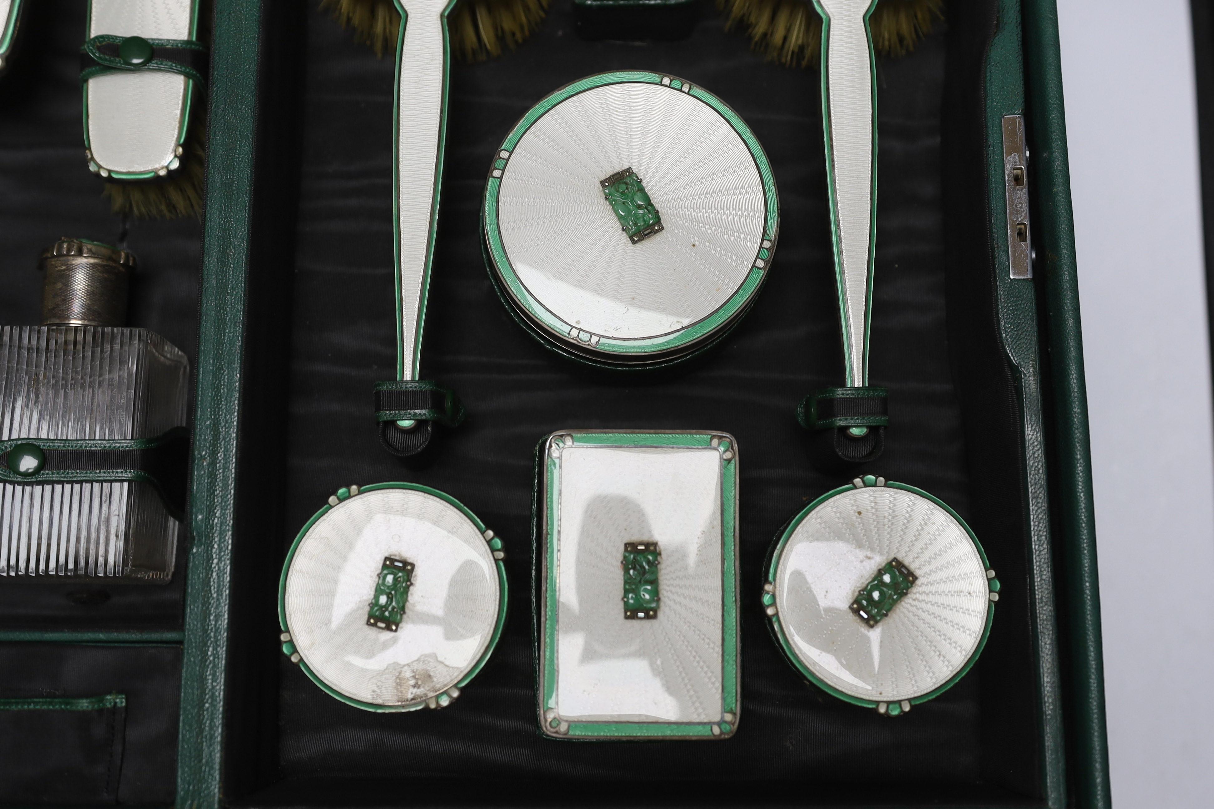 A George V silver, enamel and Chinese jadeite mounted twelve piece dressing table set, Goldsmiths & Silversmiths Co Ltd, Birmingham, 1936, housed in green leather travelling case, case width 53cm (a.f.).